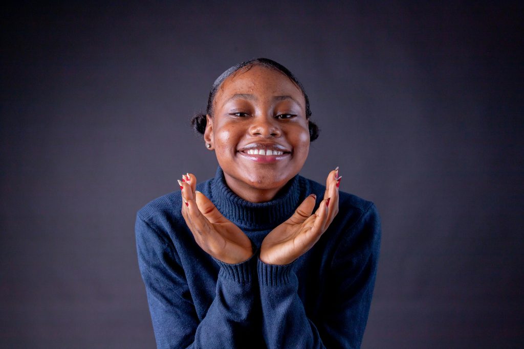 Smiling woman in a blue sweater with hands on chin, conveying happiness and warmth.